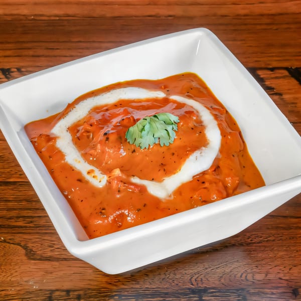 Phulkari Indian Cuisine's butter chicken, a rich orange curry with cream swirls and cilantro, in a white bowl.