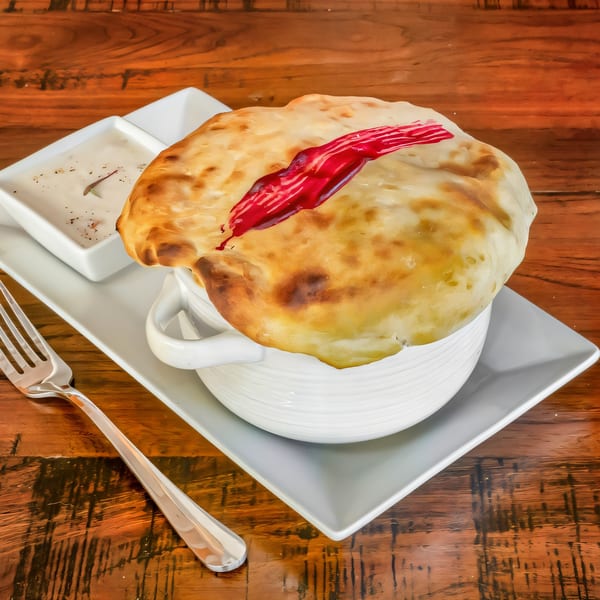 Indian dish with a baked bread crust and red sauce on top, served with a side of white sauce.