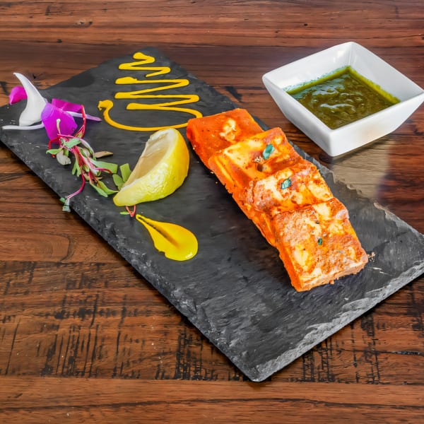 Phulkari Indian Cuisine's paneer tikka with lemon, greens, yellow sauce, and green chutney.