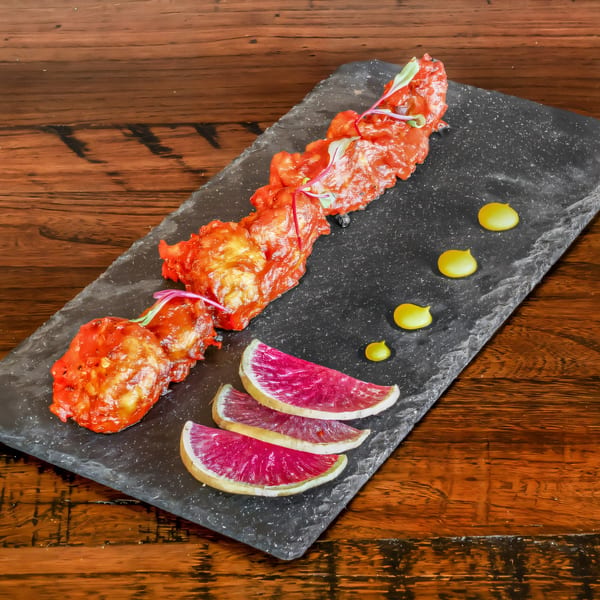 Phulkari Indian Cuisine's red chicken tikka skewers with watermelon radish and yellow sauce on a slate.