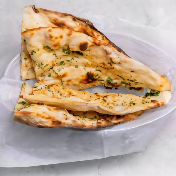 Golden brown naan bread, garnished with herbs, served on a white plate at Phulkari Indian Cuisine.