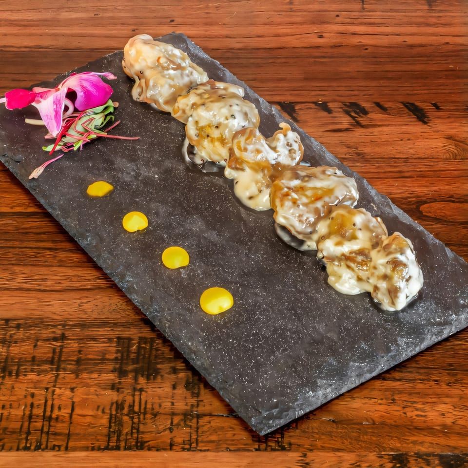 Phulkari Indian Cuisine's creamy chicken dish, garnished with a pink flower and yellow sauce dots.
