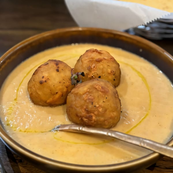 Three golden-brown fried dumplings rest in a creamy, light orange sauce with a drizzle of oil.